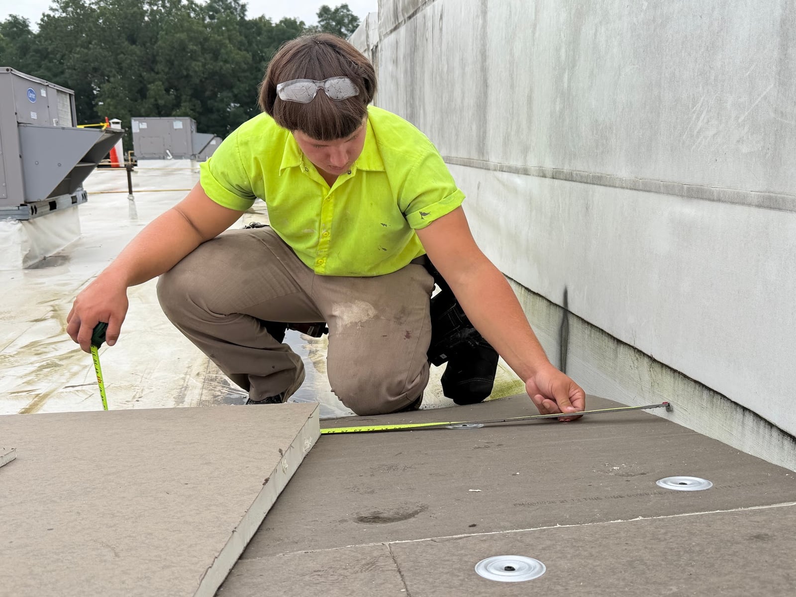 Green Improvements roofer measuring material beside a rooftop wall